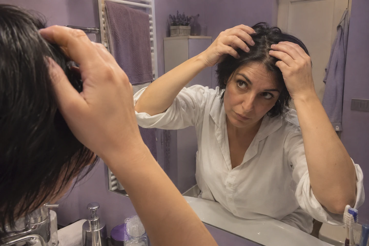 Une femme observe la raie de ses cheveux devant un miroir