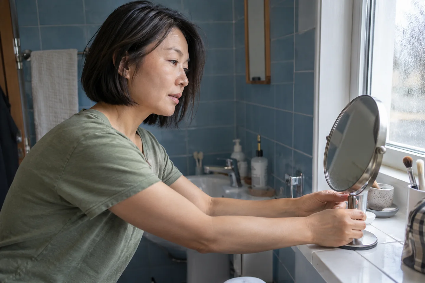 Une femme déplace son miroir près de la fenêtre