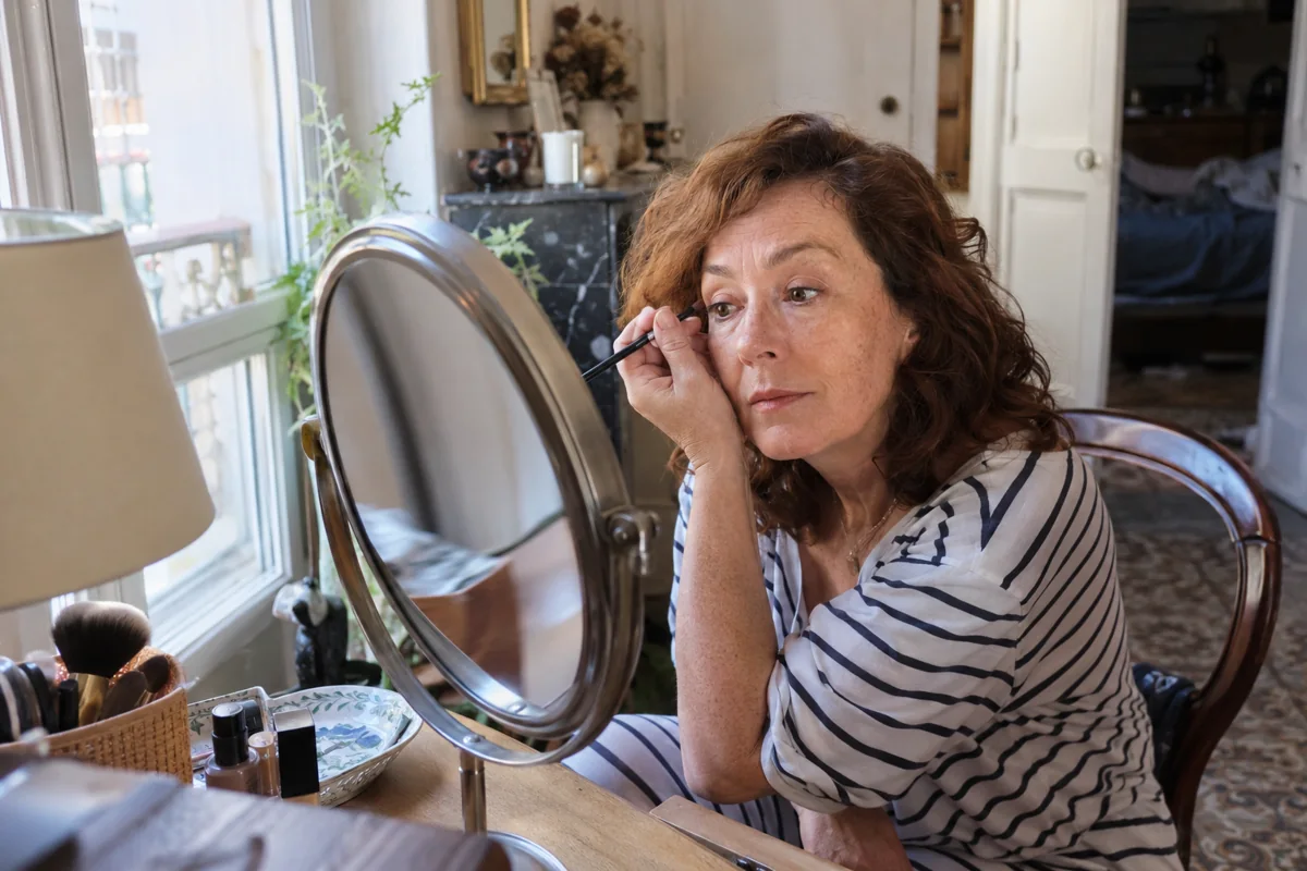 Une femme se maquille près d’une fenêtre