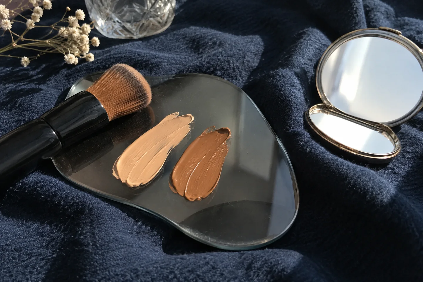 Pinceau de teint et nuances de maquillage étalées sur une palette de verre